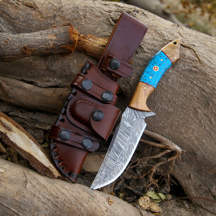 Knife with a blue blade and wooden handle in a leather sheath on a wooden surface