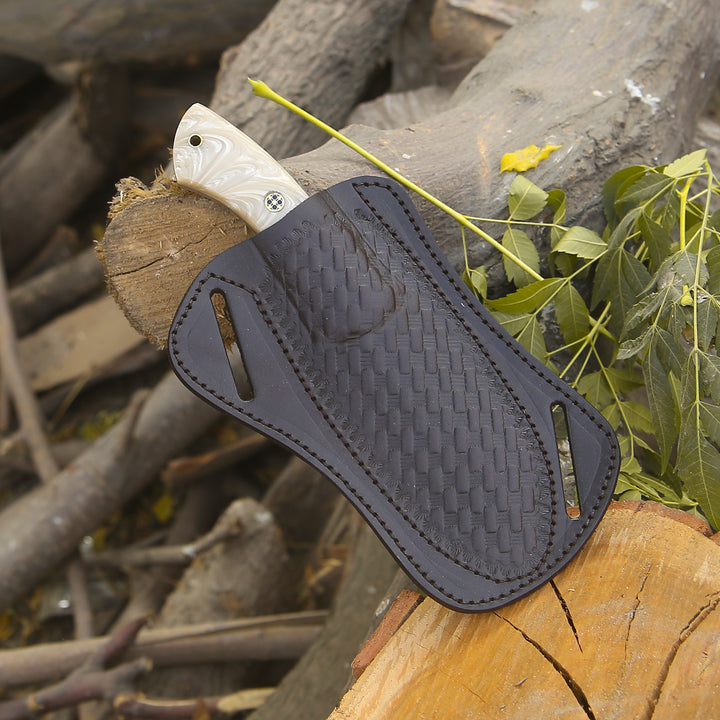 Knife with a black sheath on a wooden log with leaves in the background