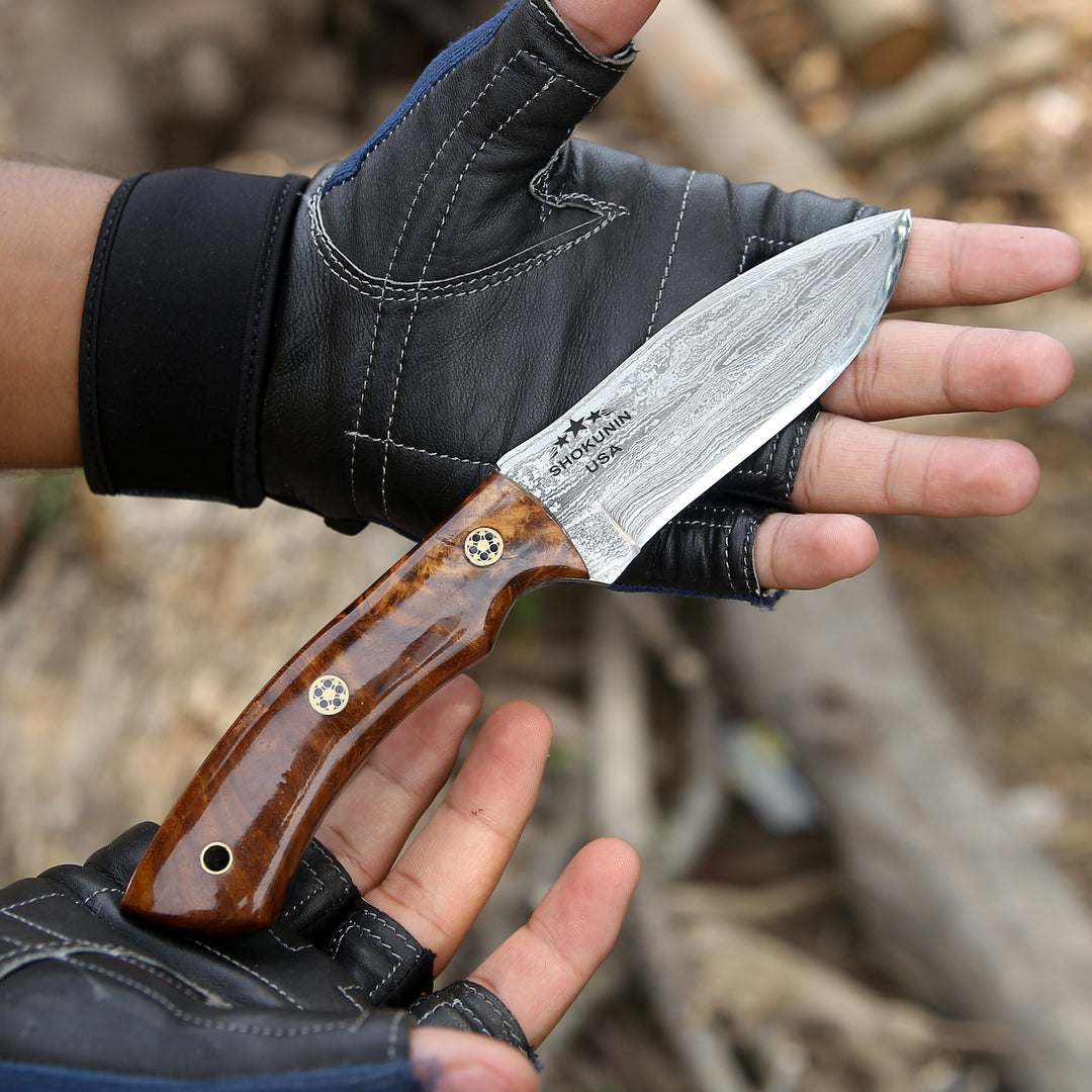 Hand holding a knife with a wooden handle and metal blade, wearing a black glove.