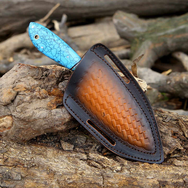 Knife with a blue handle and brown blade in a leather sheath on wooden logs.