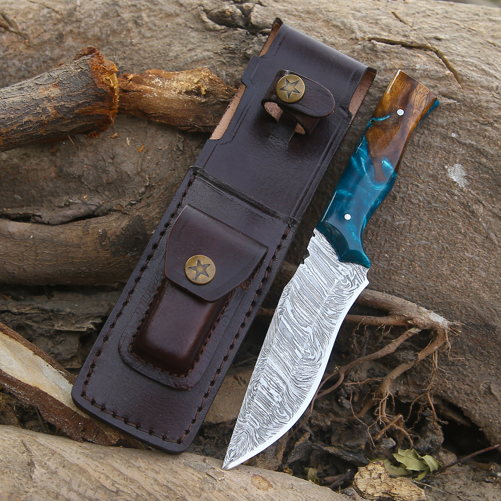Knife with a wooden handle and blue blade in a leather sheath on a rocky surface