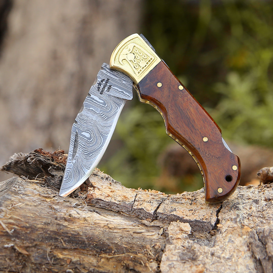 Foldable knife with a wooden handle and gold blade cover on a wooden log