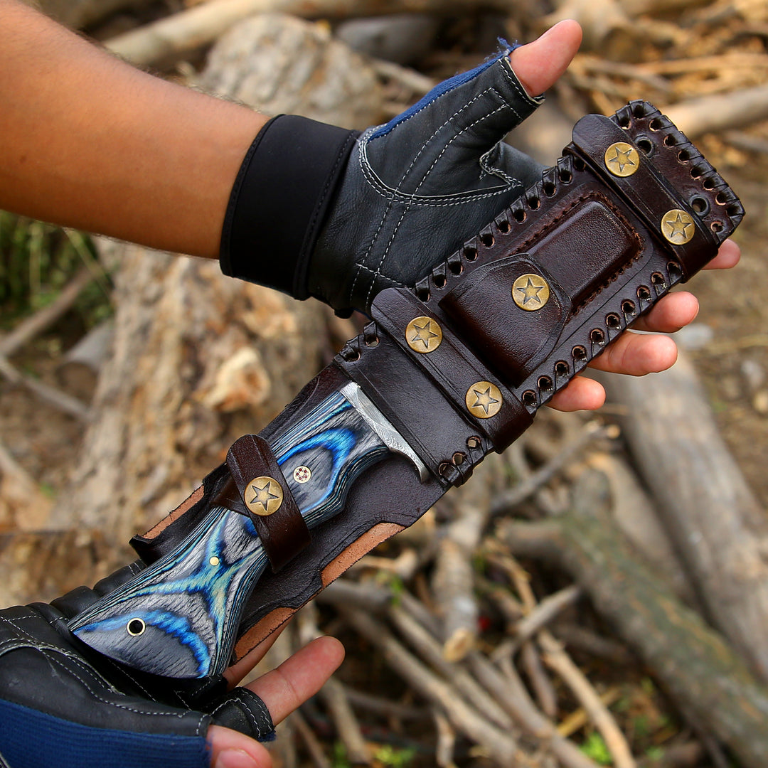 Hand holding a detailed leather glove with blue decorative elements against a natural background.